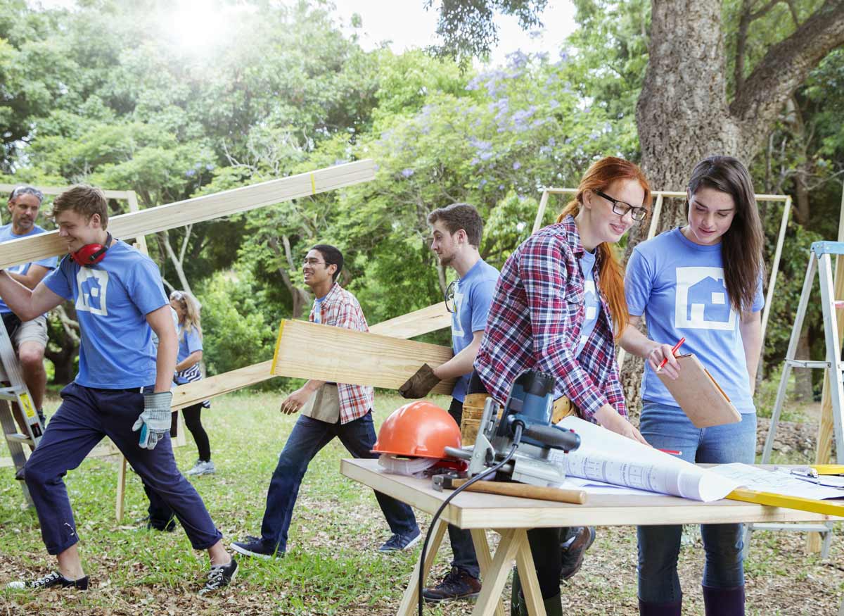 Housing volunteers cutting wood beam and transporting them across the yard.